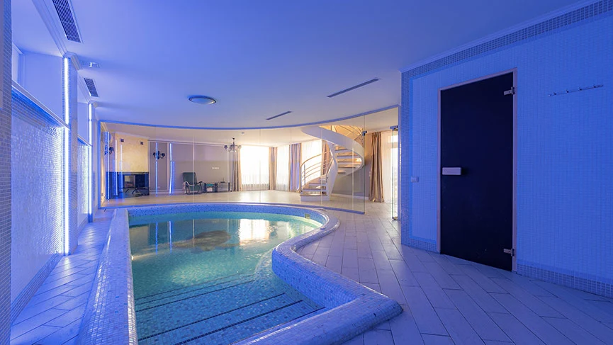 Piscina interna com linhas curvas, em um interior sofisticado predominantemente branco 